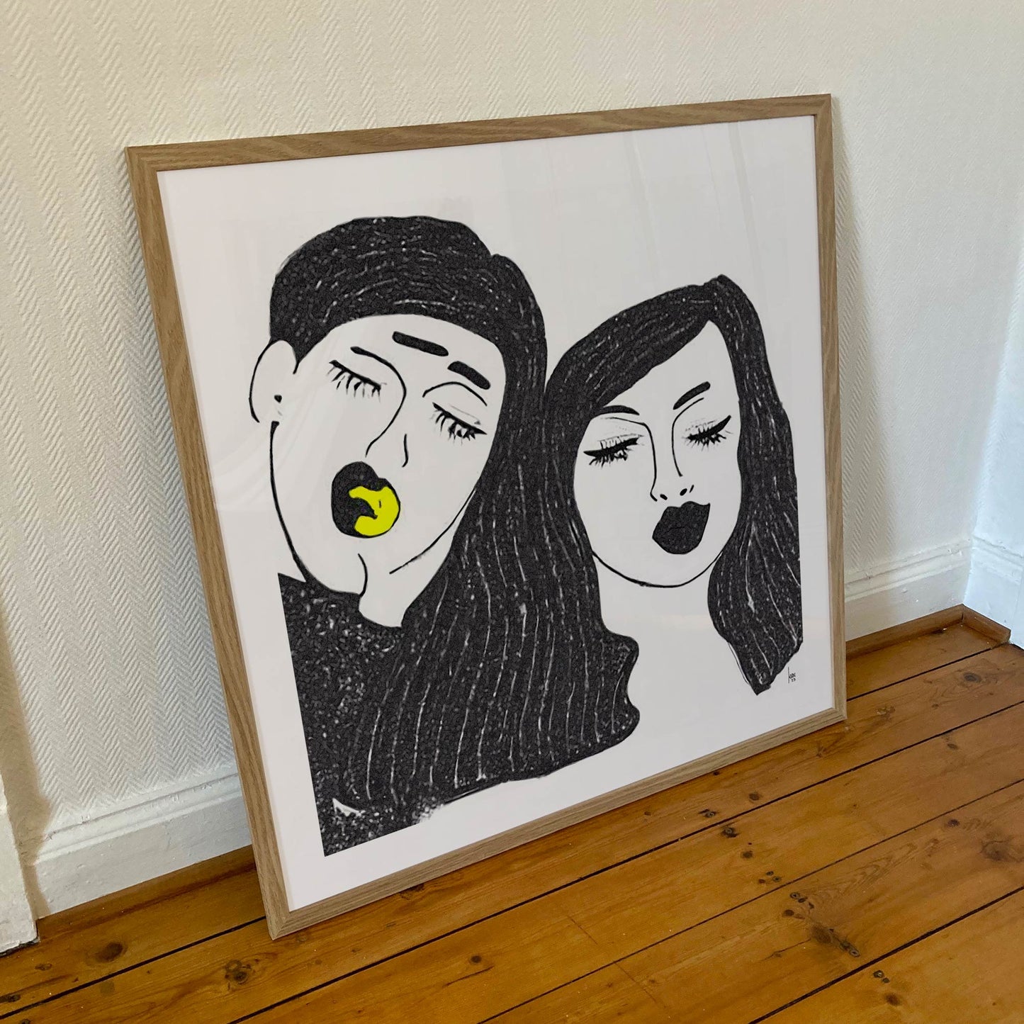 Œuvre 'TRISTAN ET YSEULT' encadrée en 70x70cm, visages enlacés en noir et blanc avec jaune, cadre en bois clair, style minimaliste moderne, 2023