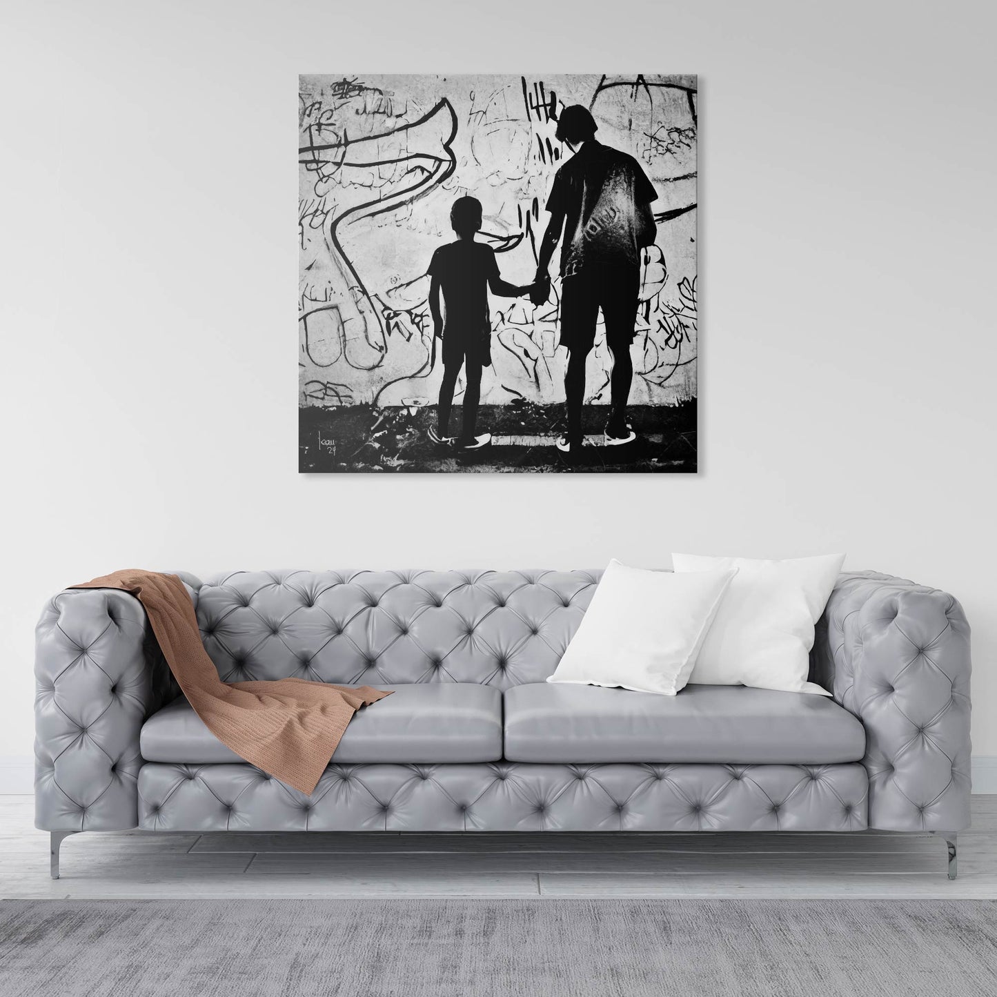 Œuvre "Paternité" exposée dans un intérieur contemporain, tableau en noir et blanc d’un adulte et d’un enfant unis par la main, devant un mur urbain expressif.